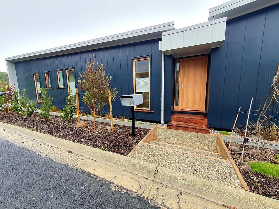 Dark blue clad home with a cedar entry door and new planting