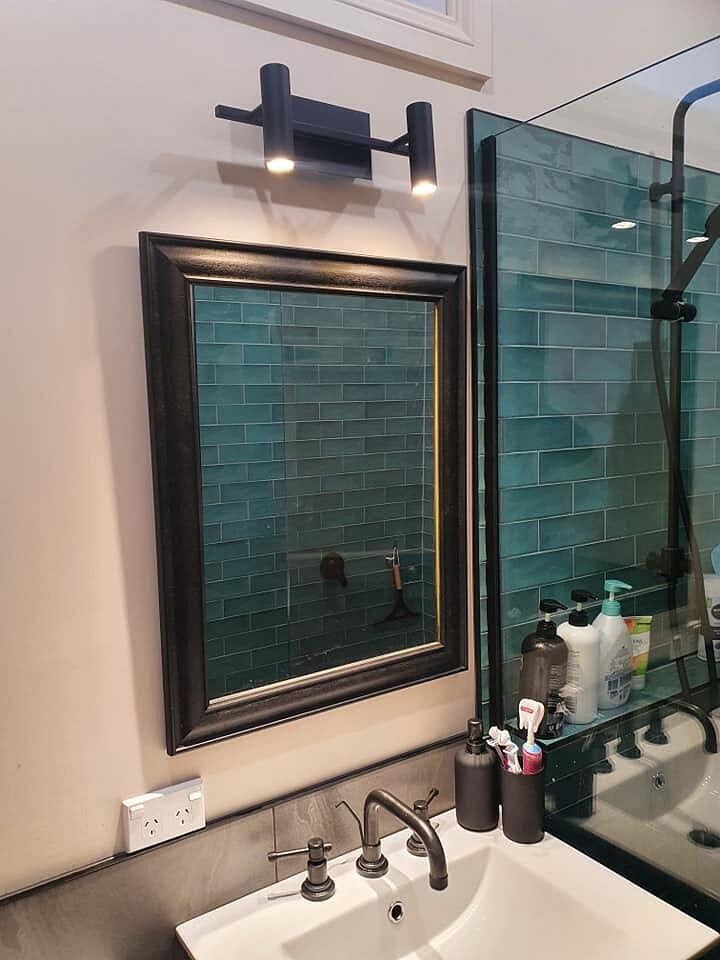 Bathroom with green subway tile behind a framed mirror